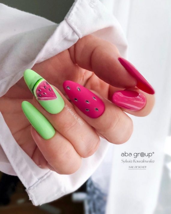 Almond-shaped nails with watermelon-inspired pink and green polish and seed nail art