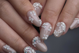 Almond-shaped bridal nails with nude polish, 3D carved white flowers, pearls, and rhinestone accents in an elegant floral design.