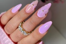Almond-shaped nails in pastel pink with glossy finish, featuring 3D lavender flower accents for a romantic spring manicure.