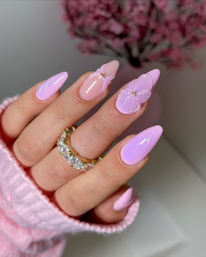 Almond-shaped nails in pastel pink with glossy finish, featuring 3D lavender flower accents for a romantic spring manicure.