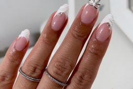 Almond nails with nude pink base, white marble French tips, and 3D silver bow accent