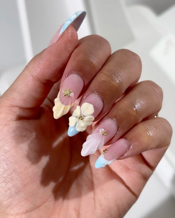Almond nails with pink base, 3D shells and flower details, pastel blue tips, and gold starfish charms