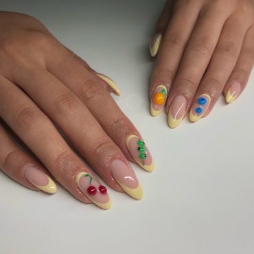 Almond nails with nude base, yellow French tips, and 3D sculpted fruits like cherries, oranges, and blueberries
