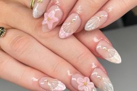 Almond-shaped nude nails with pink 3D starfish, white shell patterns, and gold accents, styled in a beach-inspired summer nail design.