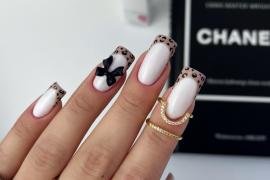 Long square nails with nude base, French leopard-print tips, and a black 3D bow accent on the ring finger.
