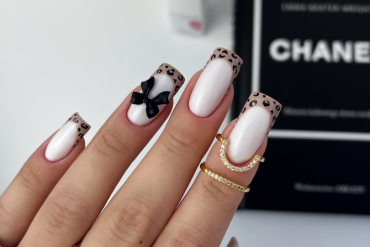 Long square nails with nude base, French leopard-print tips, and a black 3D bow accent on the ring finger.