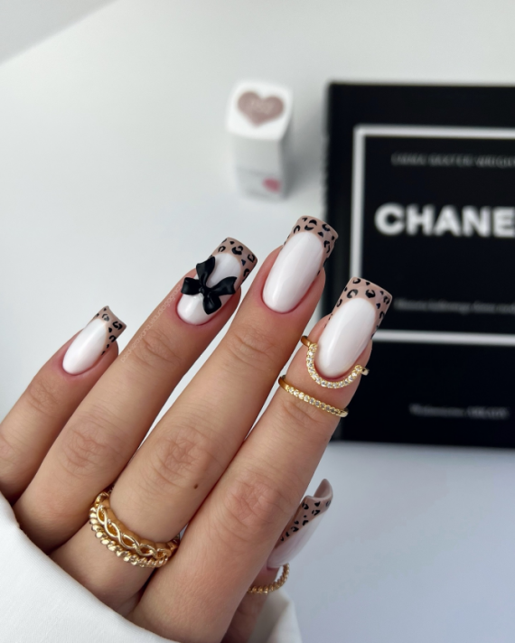 Long square nails with nude base, French leopard-print tips, and a black 3D bow accent on the ring finger.