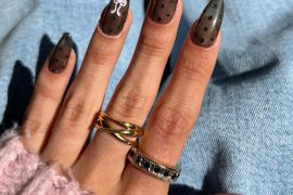 Almond-shaped nails with sheer black polish, tiny black glitter dots, and a white bow design for a Parisian-inspired manicure