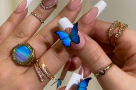 Long square nails with nude base, white French tips, and 3D electric blue butterfly decorations