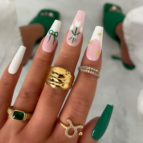 Long coffin nails with white and nude pink base, tulip and bow art, and gold stud embellishments