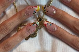 Almond-shaped nude nails with glossy colorful French tips and multicolored gemstone accents for a playful, artistic look