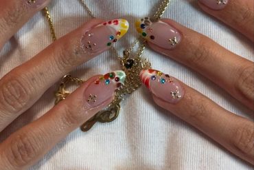 Almond-shaped nude nails with glossy colorful French tips and multicolored gemstone accents for a playful, artistic look