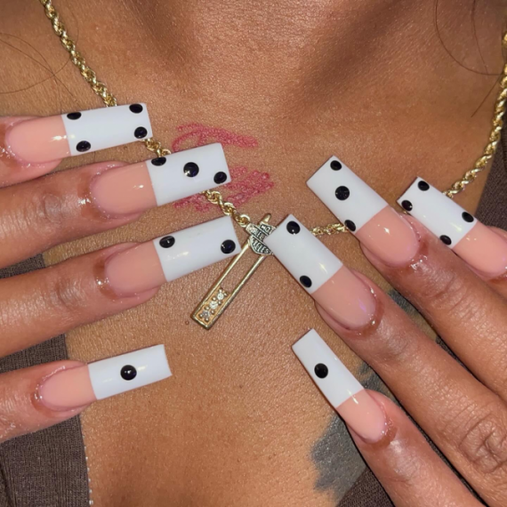 Long square acrylic nails with nude bases, white tips, and black dot accents inspired by domino tiles for a bold, graphic nail design.