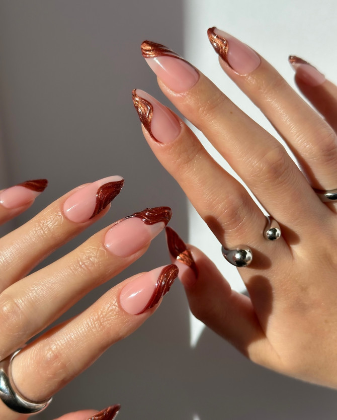 Almond-shaped nails with nude base and metallic copper swirl French tips, perfect for fall