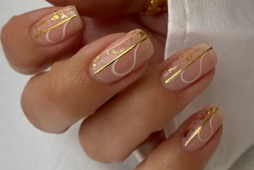Short nude nails with gold foil, minimal white line art, and glossy finish Nude square nails with gold foil flakes and minimal white swirl lines for a chic summer style