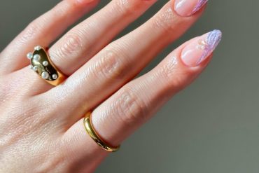 Almond-shaped nails with nude base, iridescent lilac waves, and small pearl accents