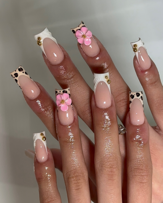 Coffin-shaped nails with nude base, leopard print French tips, 3D pink flowers, gold studs, and white swirl details.
