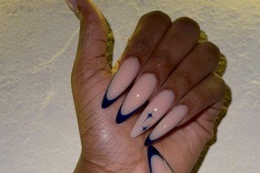 Nude almond-shaped nails with deep midnight blue French tips and a small celestial star accent