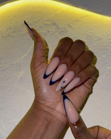 Nude almond-shaped nails with deep midnight blue French tips and a small celestial star accent