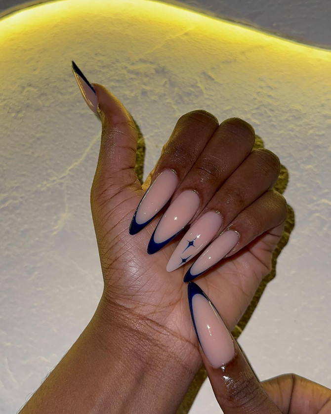 Nude almond-shaped nails with deep midnight blue French tips and a small celestial star accent