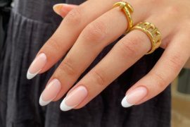 Almond-shaped nails with nude pink base and crisp white French tips, styled with gold rings