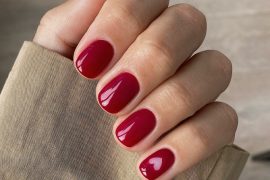 Short round nails painted in glossy cherry red with a small heart-shaped negative space detail on the ring finger