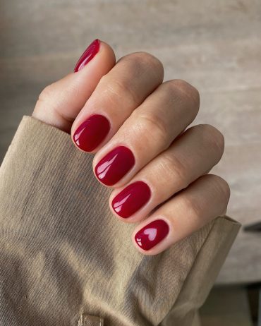 Short round nails painted in glossy cherry red with a small heart-shaped negative space detail on the ring finger