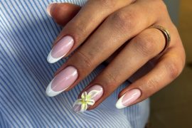 Almond-shaped nails with pink base and white French tips, featuring a 3D white flower accent on the ring finger