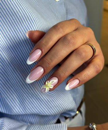 Almond-shaped nails with pink base and white French tips, featuring a 3D white flower accent on the ring finger