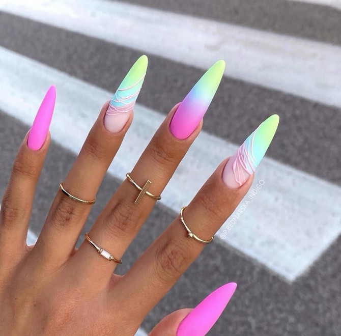 Long stiletto nails with neon ombre matte finish in pink, green, blue, and purple gradient, featuring swirl line art on two nails.