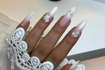Almond-shaped French ombré nails with nude to white gradient and 3D pearl flower accents