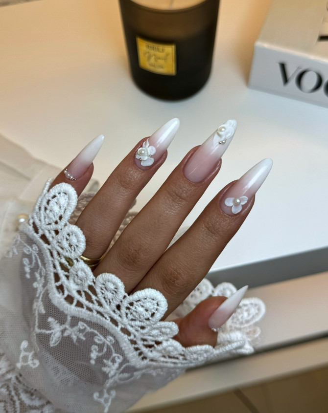 Almond-shaped French ombré nails with nude to white gradient and 3D pearl flower accents
