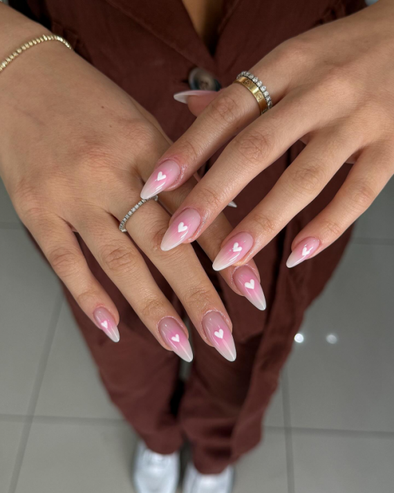 Almond-shaped nails with pink-to-white ombré gradient and small white heart accents on each nail, glossy finish.