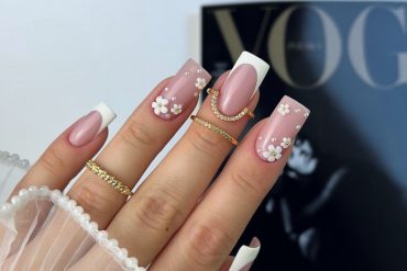 Square nude-pink nails with white French tips and 3D daisy floral accents on two fingers, decorated with tiny gold centers.