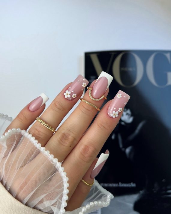 Square nude-pink nails with white French tips and 3D daisy floral accents on two fingers, decorated with tiny gold centers.