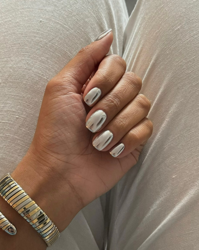 Short rounded nails with high-shine silver mirror chrome finish, worn with metallic bracelet