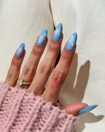 Almond-shaped soft blue aura nails with minimalist white bow, star, and floral line art designs