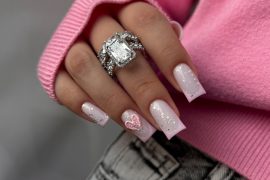 Square-shaped baby pink nails with glitter and 3D heart accent on ring finger