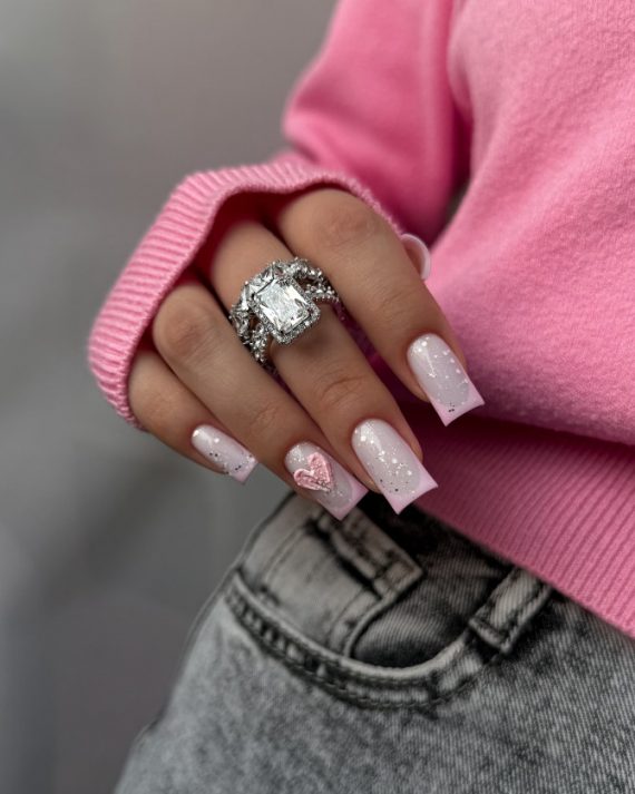 Square-shaped baby pink nails with glitter and 3D heart accent on ring finger
