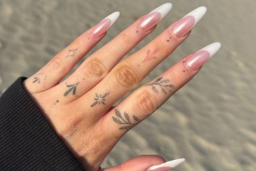 Long almond-shaped nails with nude base and classic white French tips, worn on tattooed hand