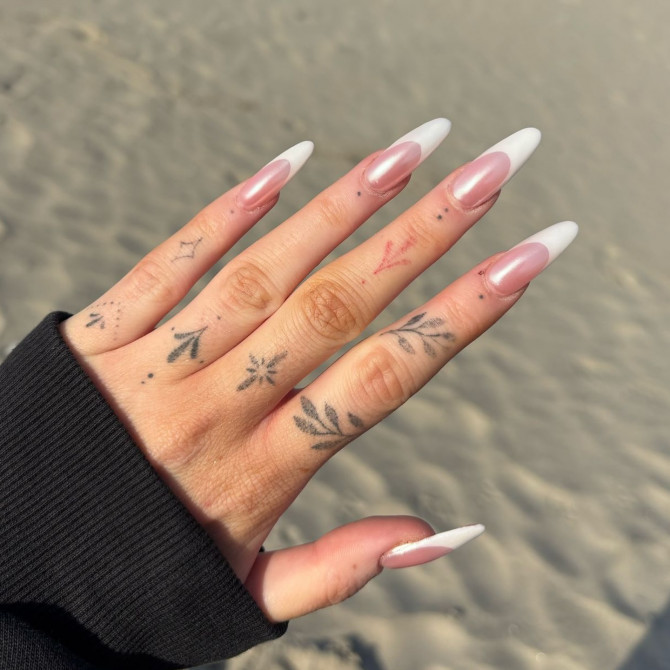 Long almond-shaped nails with nude base and classic white French tips, worn on tattooed hand