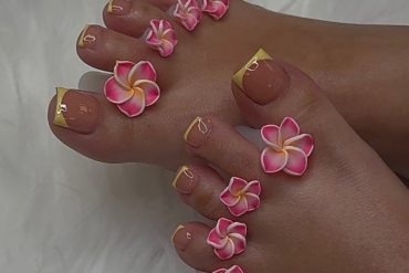 Toenails with nude polish and yellow French tips, decorated with pink and white 3D plumeria flowers on each toe.