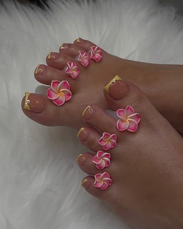 Toenails with nude polish and yellow French tips, decorated with pink and white 3D plumeria flowers on each toe.