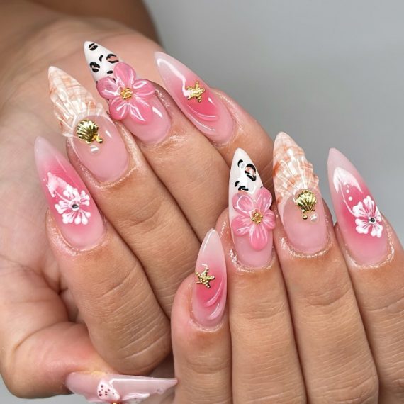 Medium stiletto nails with pink gradient, 3D flowers, seashell charms, and face art on translucent gel base
