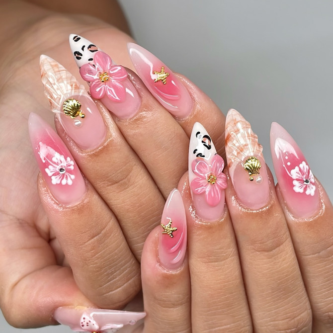 Medium stiletto nails with pink gradient, 3D flowers, seashell charms, and face art on translucent gel base
