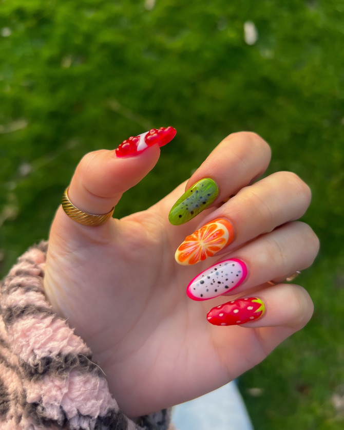 Oval nails with 3D fruit designs including strawberry, dragon fruit, orange, and kiwi in bright colors