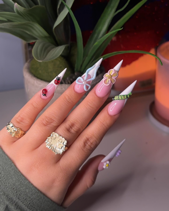Long stiletto nails with pink and white base, decorated with 3D butterfly, flowers, ladybugs, gems, and nature-inspired designs.