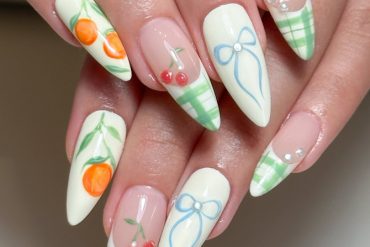 Almond-shaped pastel nails with cherries, bows, gingham tips, and orange fruit accents on a creamy white base
