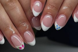 Almond-shaped French tip nails with soft pink base and miniature floral accents on two nails