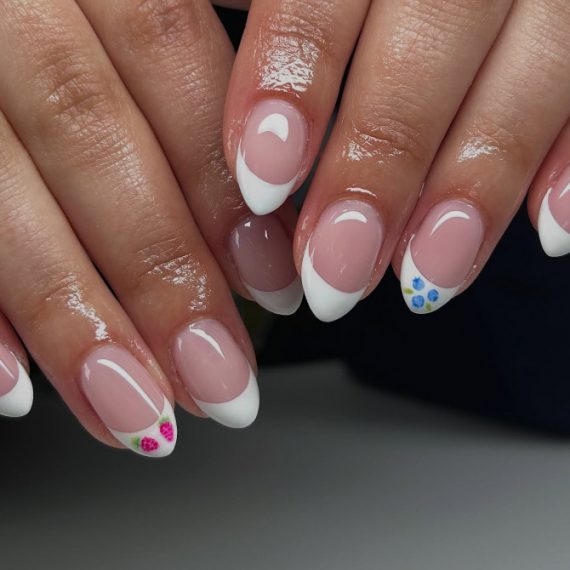 Almond-shaped French tip nails with soft pink base and miniature floral accents on two nails
